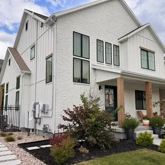 Radon mitigation system installed on a white modern farmhouse in Utah, with the vent pipe run flush against the siding and painted to blend in