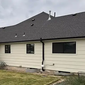 Radon mitigation system installed on a white modern farmhouse in Utah, with the vent pipe run flush against the siding and painted to blend in