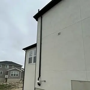 Radon mitigation system installed on a white modern farmhouse in Utah, with the vent pipe run flush against the siding and painted to blend in