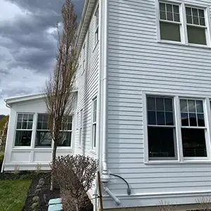 Radon mitigation system installed on a white modern farmhouse in Utah, with the vent pipe run flush against the siding and painted to blend in