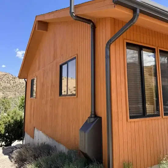 Radon mitigation system installed on a white modern farmhouse in Utah, with the vent pipe run flush against the siding and painted to blend in
